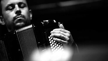 Portrait en noir et blanc de Jonas Kocher jouant de l'accordéon. Ses mains sont concentrées sur les touches, exprimant l'intensité et la concentration de la performance musicale.