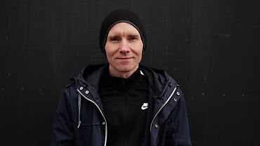 Porträt von Levin Westermann, der eine schwarze Jacke und eine dunkle Mütze trägt, vor einer schwarzen Wand stehend. Er lächelt leicht und schaut direkt in die Kamera.