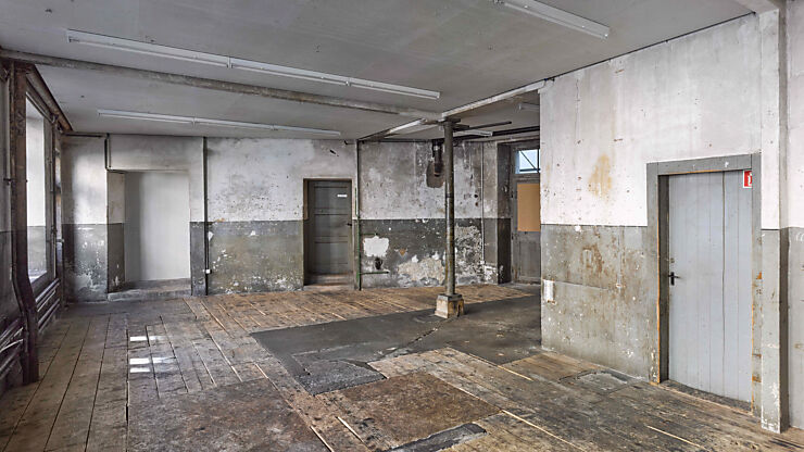 Vom hinteren Teil des Lokals aus sind im leeren Veranstaltungsraum ein alter Holzboden, unverputzte Wände und auf der rechten Seite eine freistehende Säule zu sehen.