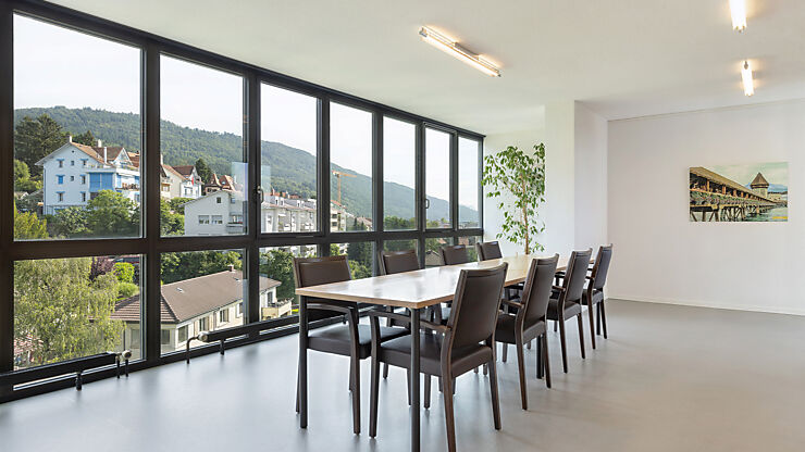 Eine Innenaufnahme vom Speisesaal im Pflegeheim mit einem Tisch und 8 Stühlen vor der Fensterfront mit Aussicht in Richtung Bözingenberg.
